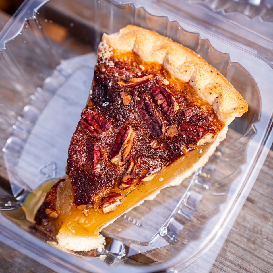 A slice of Supreme Barbecue's pecan pie with a golden crust and gooey filling in a plastic container.