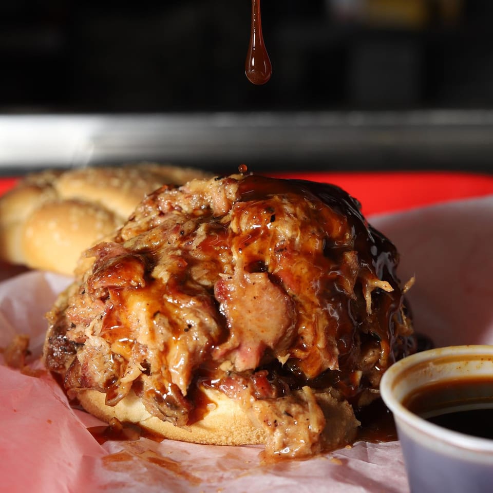 Supreme Barbecue pulled pork sandwich with barbecue sauce dripping onto it, next to a sauce cup.