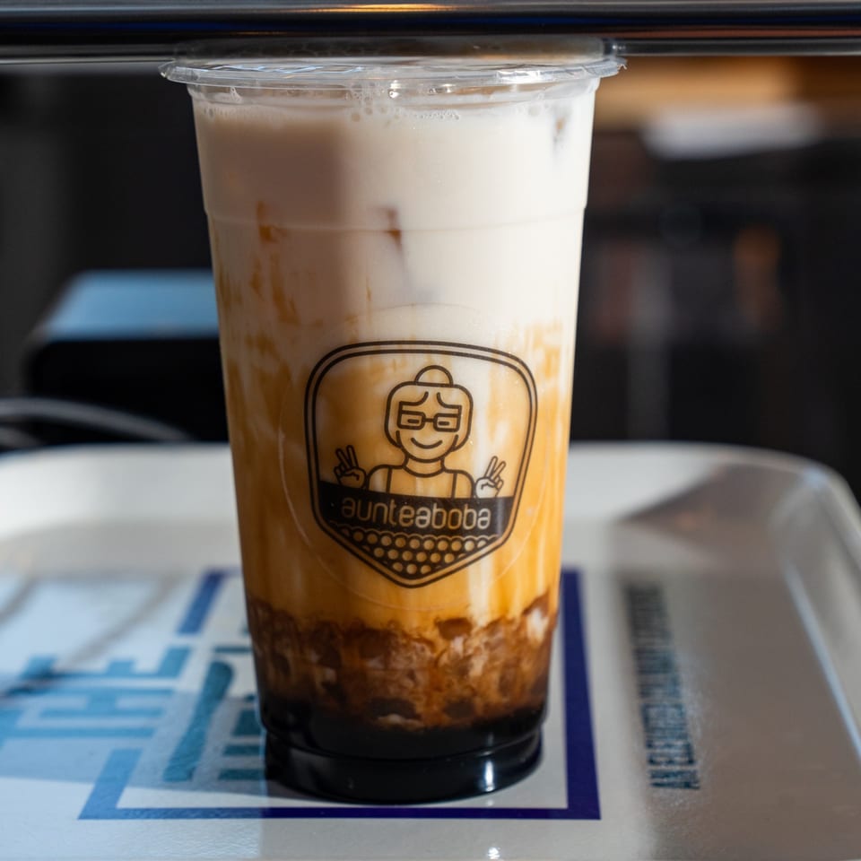 A plastic cup of layered brown sugar boba tea with the Aunteaboba logo on a white tray.