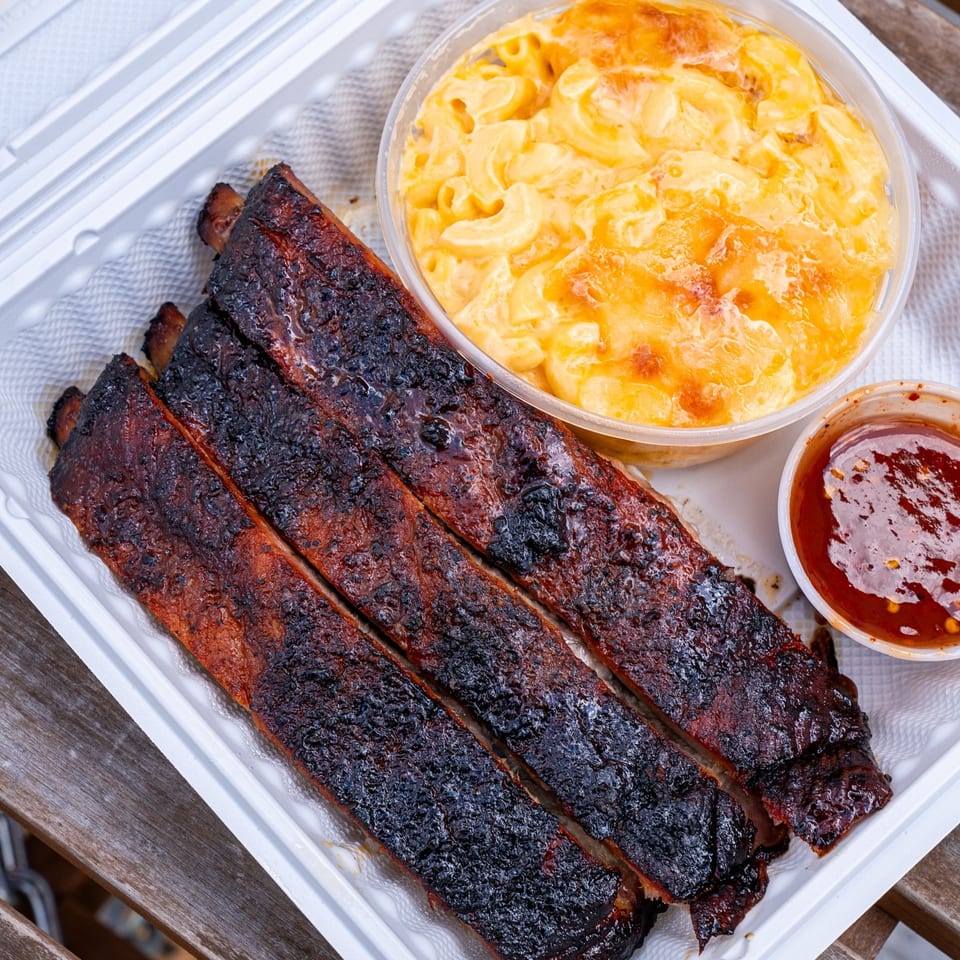 Supreme Barbecue ribs, mac and cheese, and dipping sauce in a takeout container.