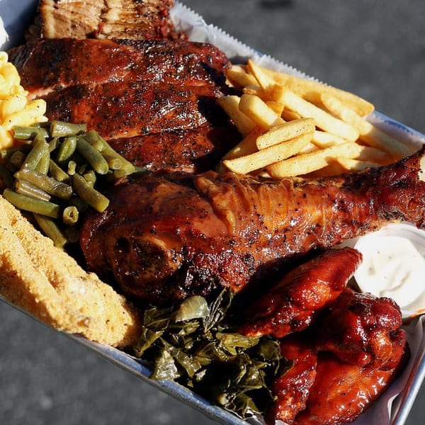 A Supreme Barbecue platter with ribs, turkey leg, wings, fries, mac and cheese, green beans, and collard greens.