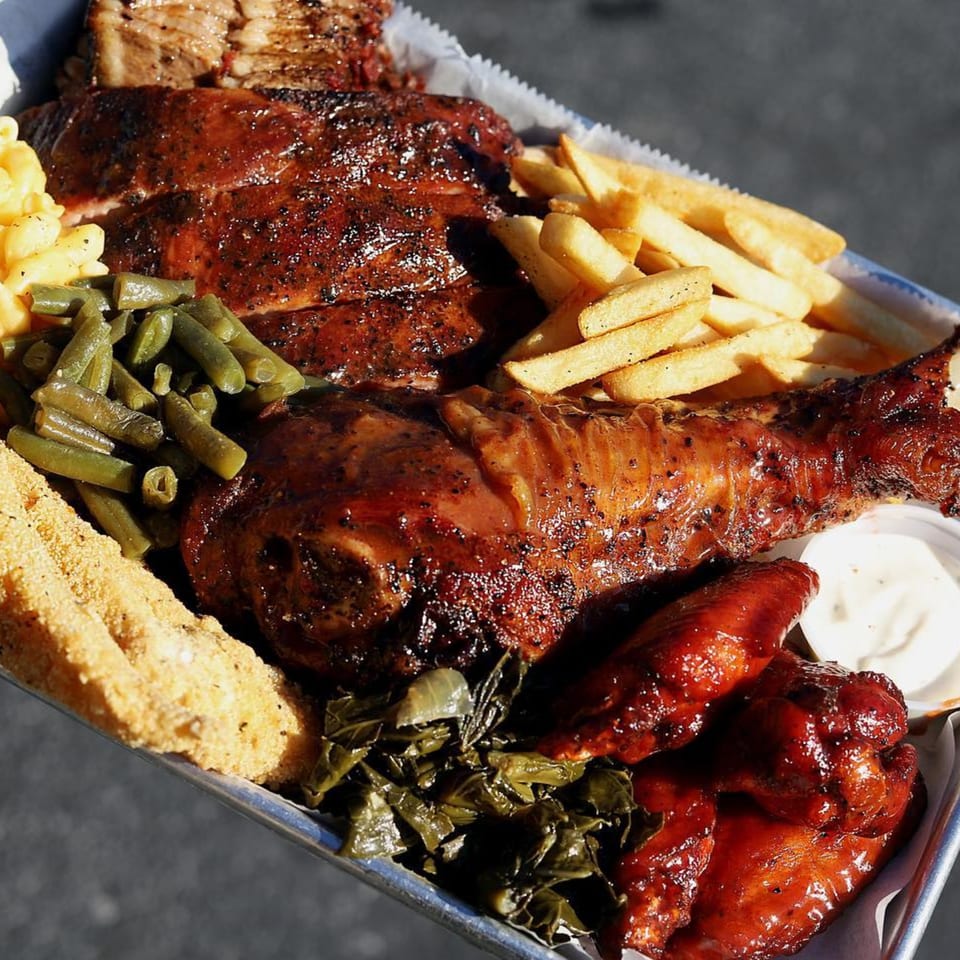 A Supreme Barbecue platter with ribs, turkey leg, wings, fries, mac and cheese, green beans, and collard greens.