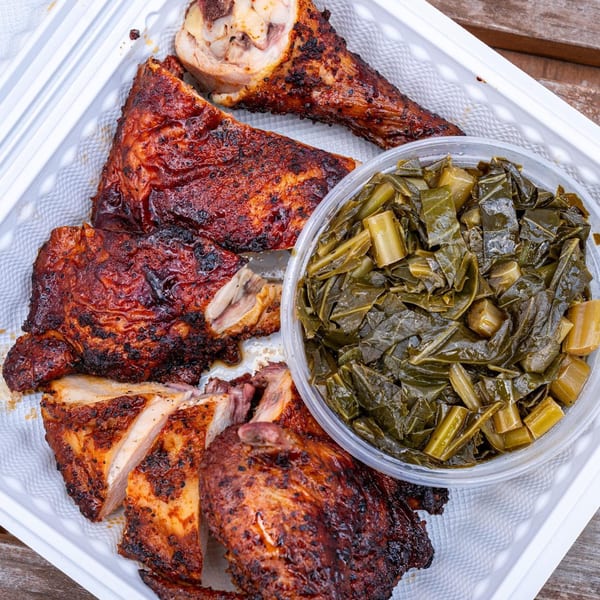 Supreme Barbecue's smoked chicken and collard greens in a white takeout container on a wooden table.