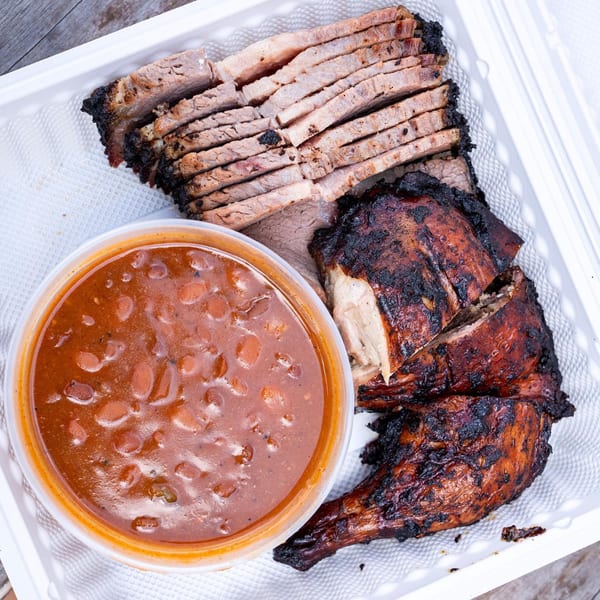 Supreme Barbecue platter with sliced brisket, grilled chicken, and a side of baked beans.
